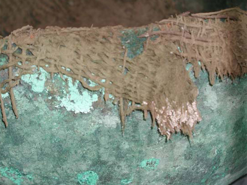 Εικ. 1. Λεπτομέρεια από ταφικό σύνολο που περιλαμβάνει
ύφασμα. Απεικονίζεται μέρος του χάλκινου αγγείου που έρχεται σε επαφή με ύφασμα.