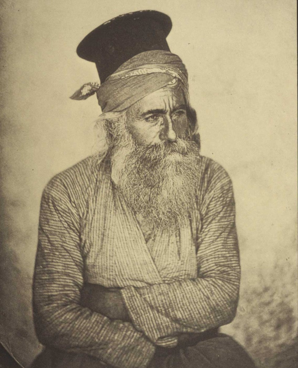 Ο ιερέας του χωριού Αυγόρου. Στο καλυμμαύχι έχει σταμπωτό δεμένο μαντήλι. Φωτ. John Thomson, 1878.