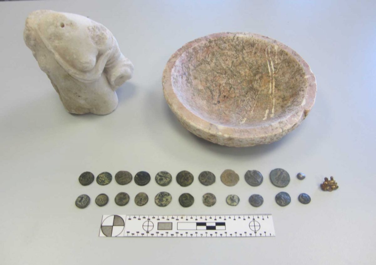 Βρέθηκαν 21 χάλκινα νομίσματα, ένας μαρμάρινος κορμός γυναικείου αγάλματος, ένα μολύβδινο σφαιρίδιο, ένα μεταλλικό διακοσμητικό αντικείμενο και μία ρηχή λεκάνη από ασβεστολιθικό πέτρωμα (φωτ.: Ελληνική Αστυνομία).