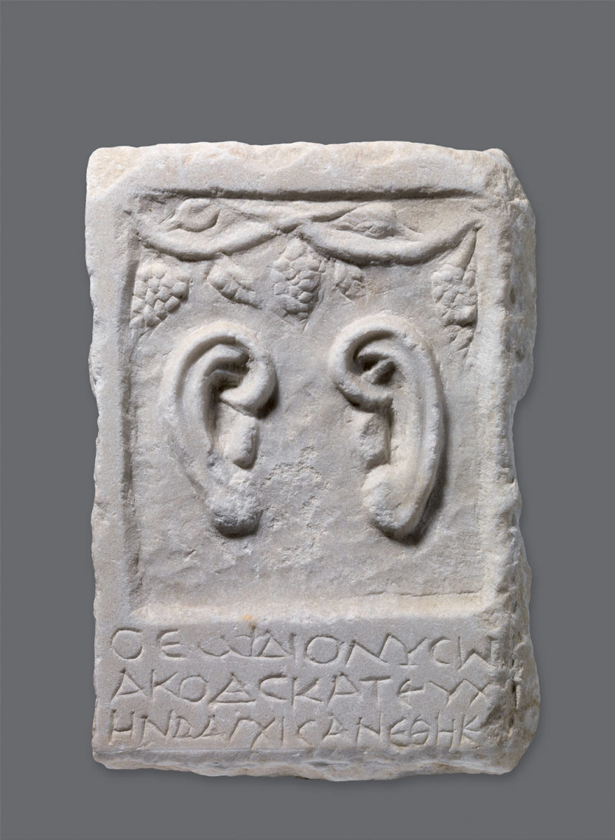 Μαρμάρινο ενεπίγραφο ανάγλυφο με παράσταση αυτιών. 2ος αι. μ.Χ. Ύψ. 29 εκ., πλ. 20 εκ. Θεσσαλονίκη, Σαραπείον. Θεσσαλονίκη, Αρχαιολογικό Μουσείο.
