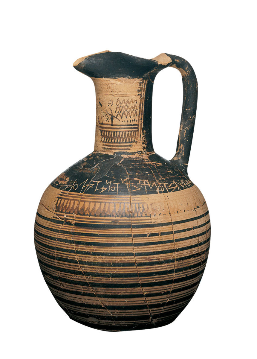 Πήλινη αττική τριφυλλόστομη οινοχόη. Στον ώμο φέρει εγχάρακτη μια από τις πρωιμότερες γνωστές ελληνικές επιγραφές. Από την Αθήνα (Δίπυλο). 750-725 π.Χ. (© TAΠΑ/Εθνικό Αρχαιολογικό Μουσείο).