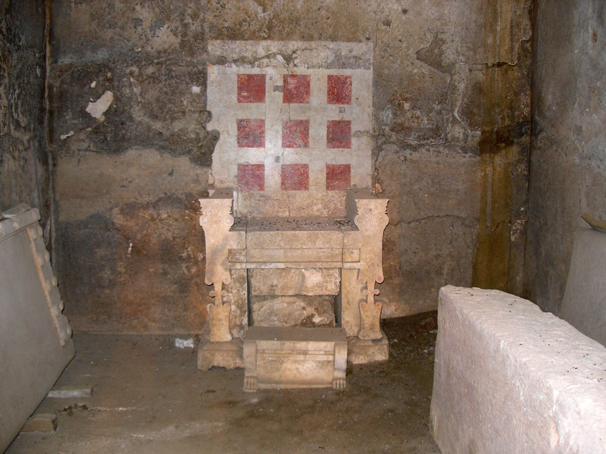 Ο θρόνος του τάφου του λεγόμενου «τύμβου Μπέλλα», στην ανατολική πλευρά του αρχαίου νεκροταφείου της Βεργίνας. Είναι εύρημα του Μ. Ανδρόνικου και του ΑΠΘ το 1981. Είναι κατασκευασμένος από συναρμοσμένα μαρμάρινα μπλοκ. Η πλάτη δεν είναι πραγματική, αλλά ζωγραφισμένη στον πίσω τοίχο. Στην επιφάνεια του υποποδίου του είναι χαραγμένα τα περιγράμματα δύο πελμάτων.