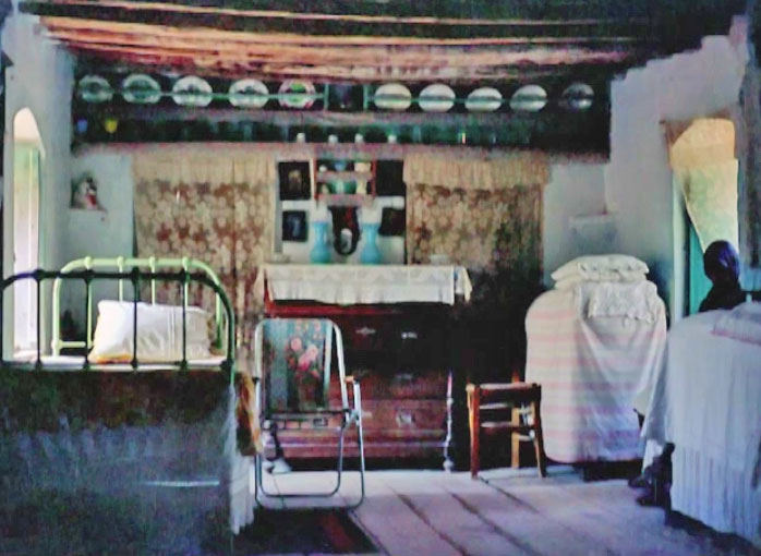 Εικ. 19. Άποψη του ίδιου εσωτερικού χώρου στο κυρίως σπίτι, με το πατάρι ύπνου - Βορειοδυτικός τοίχος. Φωτογραφία από το βίντεο «Το σπίτι του μάστορα Ροδάκη στο Μισαγρό Αίγινας» (υλικό του 1980). ©Γιάννης Τριτσιμπίδας. https://vimeo.com/34739133 (2012). Απόσπασμα 018΄-024΄. (τελευταία επίσκεψη: 1.4.2014). 