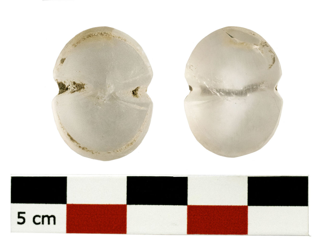 Εικ. 6. «Οικία των Θρανίων», Χώρος 1. Ψήφος από ορεία κρύσταλλο σε σχήμα οκτώσχημης ασπίδας, με κατάλοιπα ερυθρού νήματος στην οπή ανάρτησης (φωτ.: ΥΠΠΟΑ).