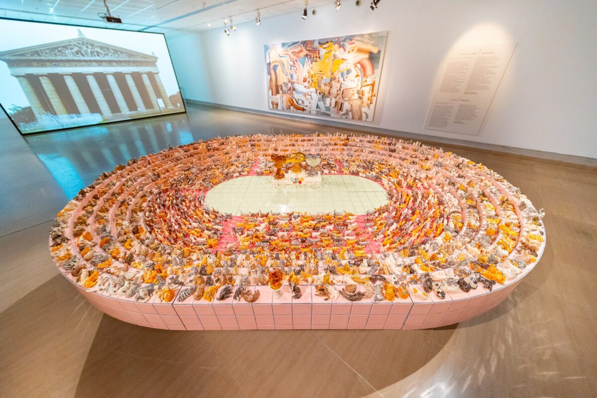 Άποψη της περιοδικής έκθεσης όπου σε πρώτο πλάνο διακρίνεται το έργο «Τελετή έναρξης των Ολυμπιακών Αγώνων για γάτες» του Νομπουάκι Τακεκάβα (2019), στον τοίχο το έργο «Επαναπατρισμός» του Κέι Ιμάτζου (2015) και στο βάθος η βιντεοεγκατάσταση «Αυθεντικότητα» του Γιου Αράκι (2016) με άμεση αναφορά στον Παρθενώνα (© ΥΠΠΟΑ/ΒΧΜ).