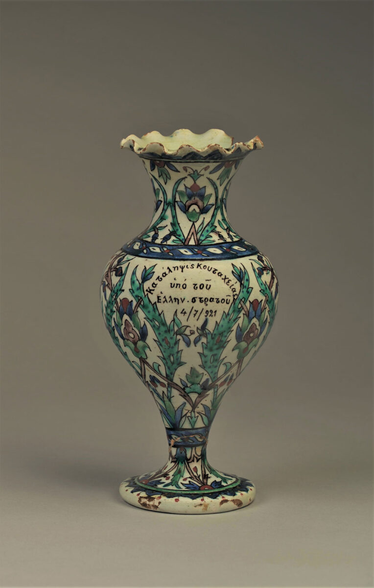 Ενεπίγραφο ανθοδοχείο με τη φράση «Κατάληψις Κουταχείας υπό του Ελλην. στρατού 4/7/921». Το κείμενο πλαισιώνεται από φύλλα σαζ που σχηματίζουν στεφάνι. Κιουτάχεια, Ιούλιος-Αύγουστος 1921. Ύψος: 22,3 εκ. Ιδιωτική συλλογή.