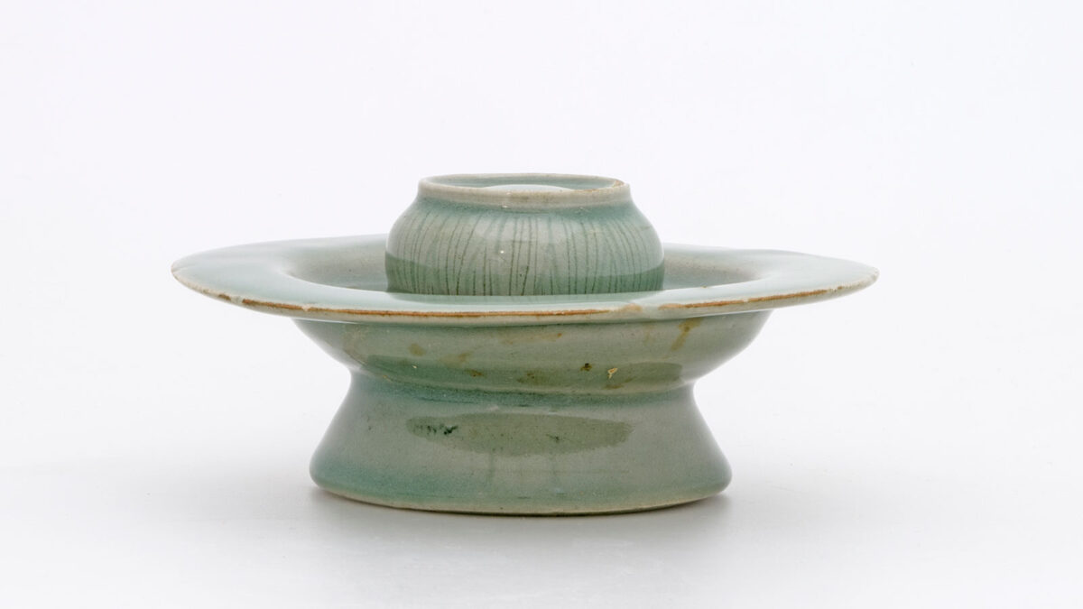 Υποστήριγμα κύπελου. Λιθοκέραμος με εγχαράξεις κάτω από πράσινη εφυάλωση: άνθη και πέταλα λωτού στην επιφάνεια έδρασης και άνθη με φύλλα στην περιφέρεια του δίσκου, η οποία επίσης φέρει εγκοπές. Κορέα. Δυναστεία Κόρυο (918-1392), 12ος αι. Διάμ. 15 εκ. Μουσείο Μπενάκη 2414. Δωρεά Γεωργίου Ευμορφόπουλου.