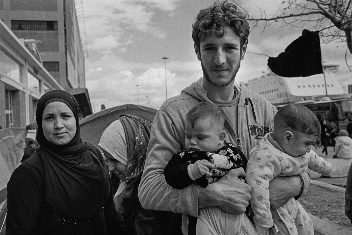 Πρόσφυγες και εθελοντής στο λιμάνι του Πειραιά, 2016. Φωτογραφία του Παναγιώτη Σωτηρόπουλου από την έκθεση «Ανώνυμες Διαδρομές» στο Μουσείο Μπενάκη / Πειραιώς 138.