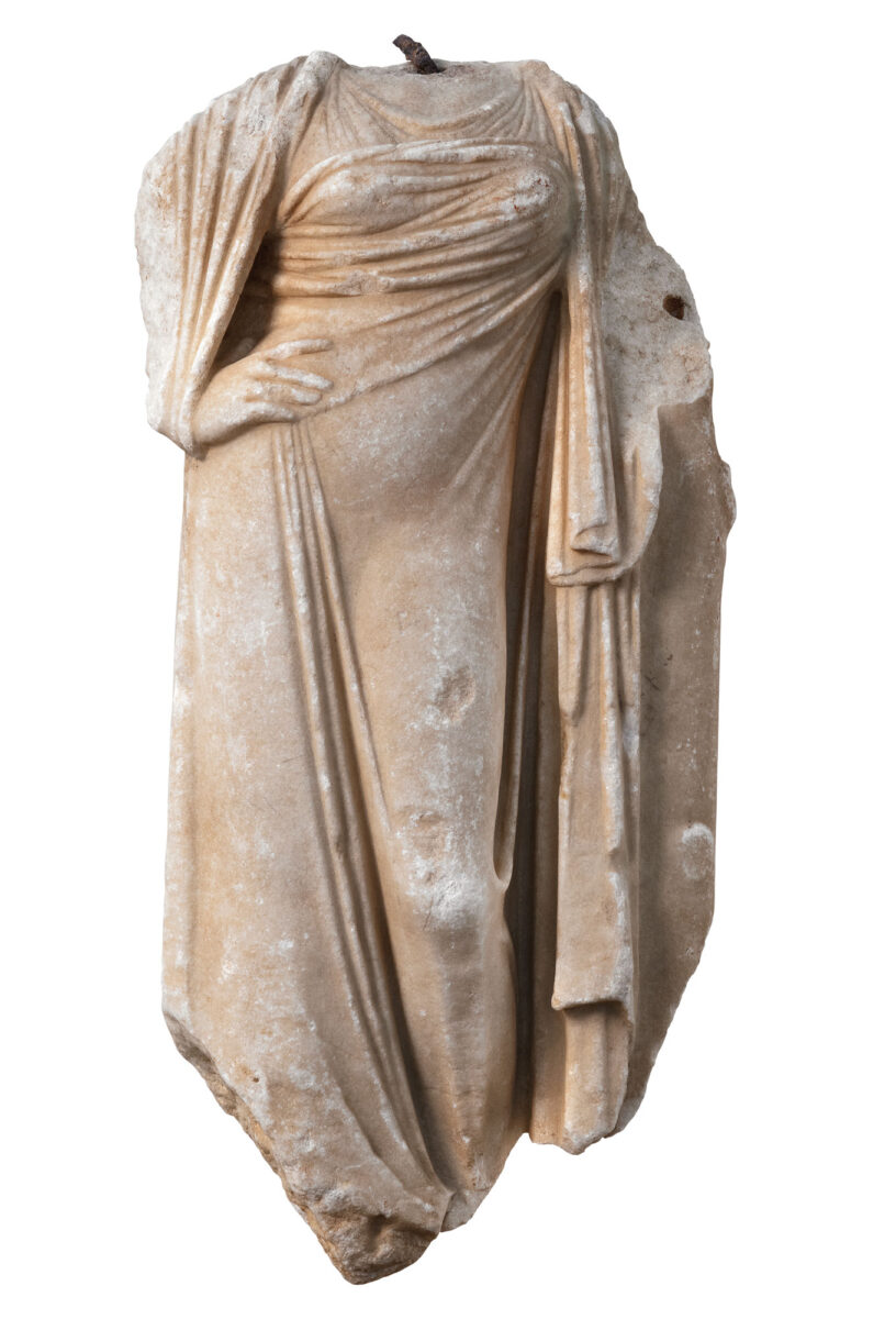 Μαρμάρινο αγαλμάτιο θεάς που με περισσή λεπτότητα και χάρη ακουμπά το χέρι στη μέση. Οι καμπύλες και η πλαστικότητα του σώματος διαφαίνονται κάτω από το λεπτό ύφασμα, με το οποίο αριστοτεχνικά αποδίδεται η ενδεδυμένη γυμνότητα της θεάς. Τριχόνειο (σημ. Γαβαλού), Ύστερη Ελληνιστική περίοδος. Φωτ.: Σωκράτης Μαυρομμάτης.