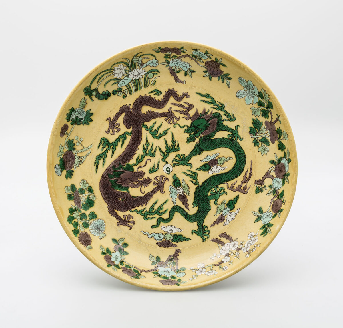 Πιάτο, πορσελάνη με εγχάρακτους δράκους, σύννεφα και ανθισμένα κλαδιά, ζωγραφισμένα με σμάλτα, επιγραφή έξι ιδεογραμμάτων εντός διπλού κύκλου σε μπλε του κοβαλτίου κάτω από την εφυάλωση, στη βάση, που μεταφράζεται ως «Φτιαγμένο στη Μεγάλη Δυναστεία Τσινγκ κατά την περίοδο του αυτοκράτορα Κανγκσί», Τσιντετζέν, Κανγκσί (1662-1722 μ.Χ.), διάμ. 35,4 εκ. Μουσείο Μπενάκη 2677, δωρεά Γεώργιου Ευμορφόπουλου.
