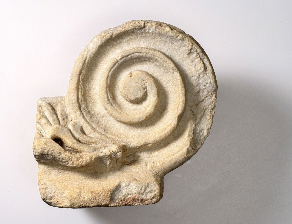 Θραύσμα μαρμάρινου ιωνικού κιονοκράνου με φερόμενη προέλευση την αρχαία Αγορά της Κορίνθου (1ος-2ος αι. μ.Χ.). Πηγή εικόνας: ΥΠΠΟ.