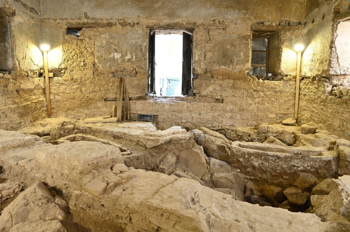 Άποψη των ευρημάτων στο εσωτερικό όπου διακρίνονται τμήματα της τοιχοποιΐας τρίκλιτης βασιλικής, μία ταφή και ο φυσικός βράχος. Πηγή εικόνας: ΥΠΠΟ.