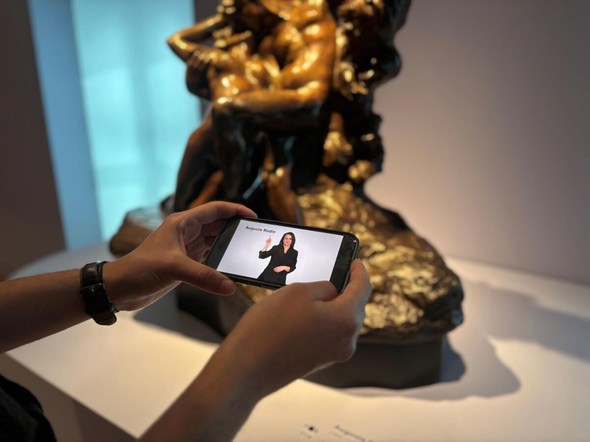 Οι επισκέπτες της μόνιμης Συλλογής του Ιδρύματος Β&Ε Γουλανδρή μπορούν να παρακολουθήσουν τις ξεναγήσεις στην Ελληνική Νοηματική Γλώσσα στους εκθεσιακούς χώρους, σκανάροντας με smartphone ή tablet τα ειδικά QR codes που βρίσκονται δίπλα στα αντίστοιχα έργα. Πηγή εικόνας: Ίδρυμα Β&Ε Γουλανδρή.